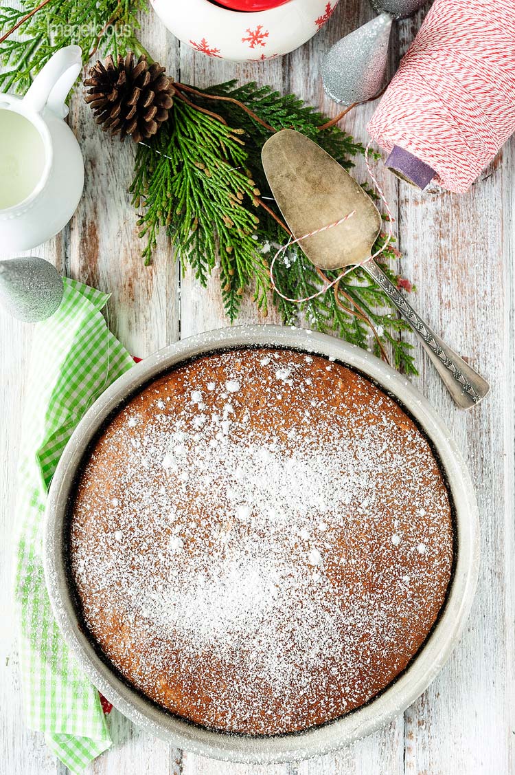 Top down view of Vegan Gingerbread Cake in a pan, covered in icing sugar. More christmas decorations are around the pan